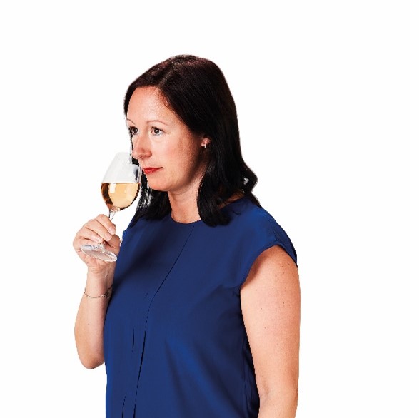 Image of woman in blue top smelling a glass of white wine
