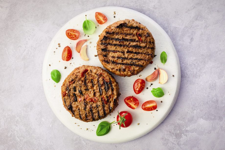 Two pizza burgers on a white plate with tomatoes and basil surrounding