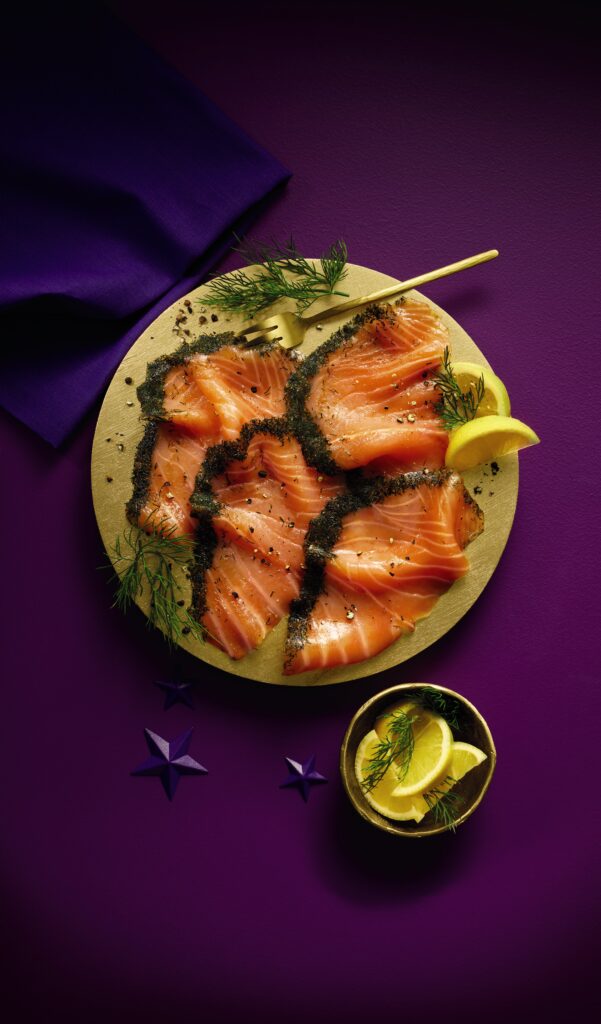 Gravadlax on a gold plate with a purple background. Lemon wedges to garnish.