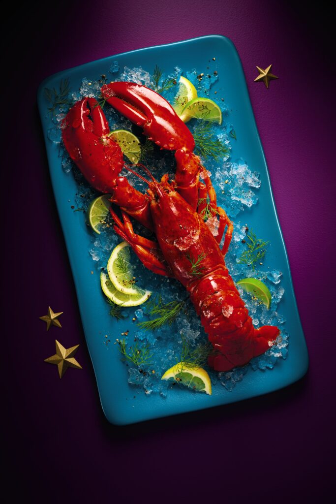 Bright red lobster on blue plate, surrounded by lemon and ice