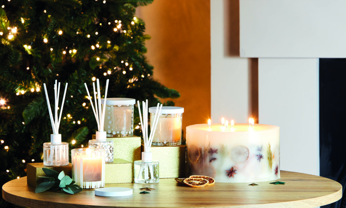 A festive living room with a Christmas tree in the background. There a a cluster of candles and diffusers on a gold table.